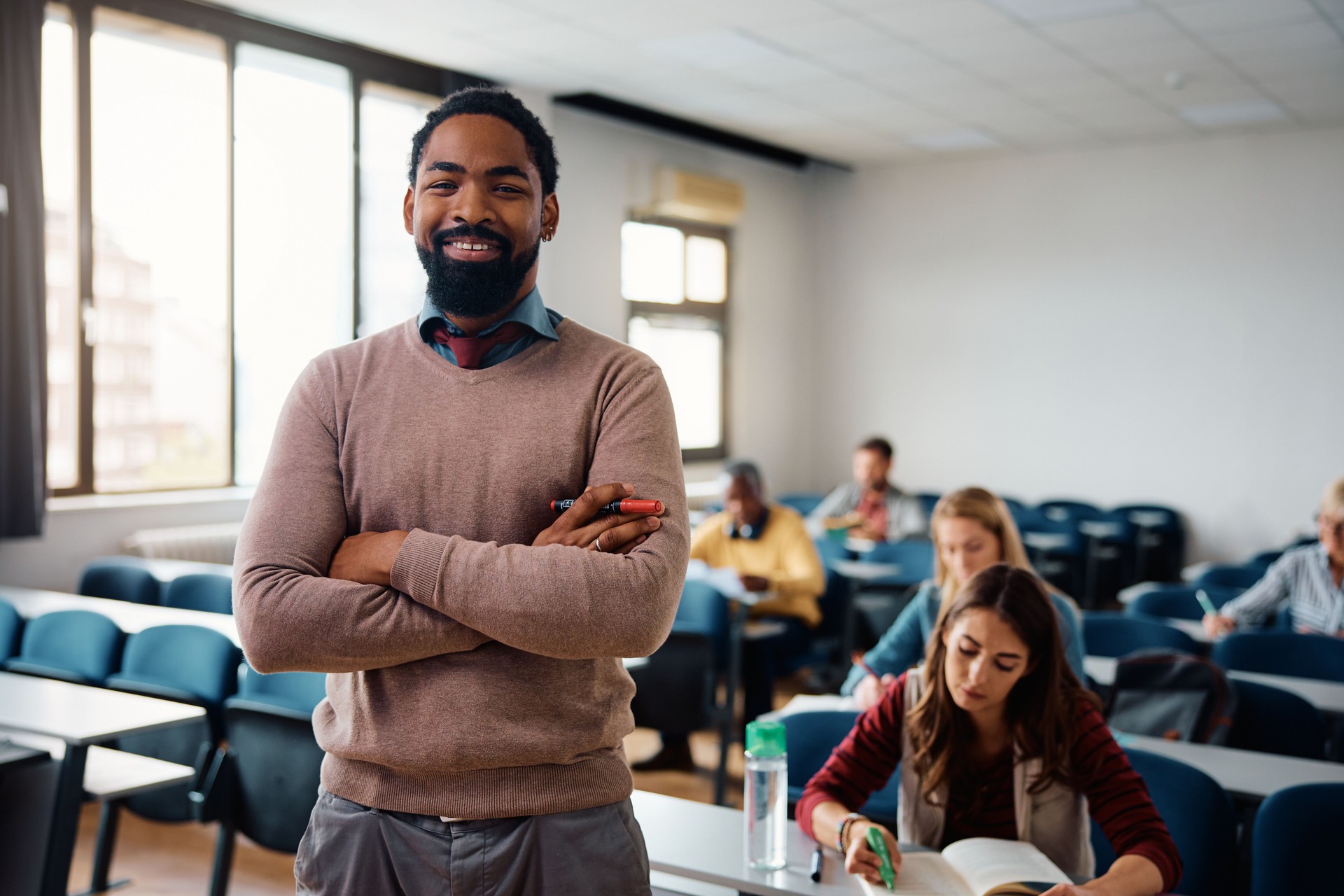 Happy black professor during a class with adult students in the classroom looking at camera.